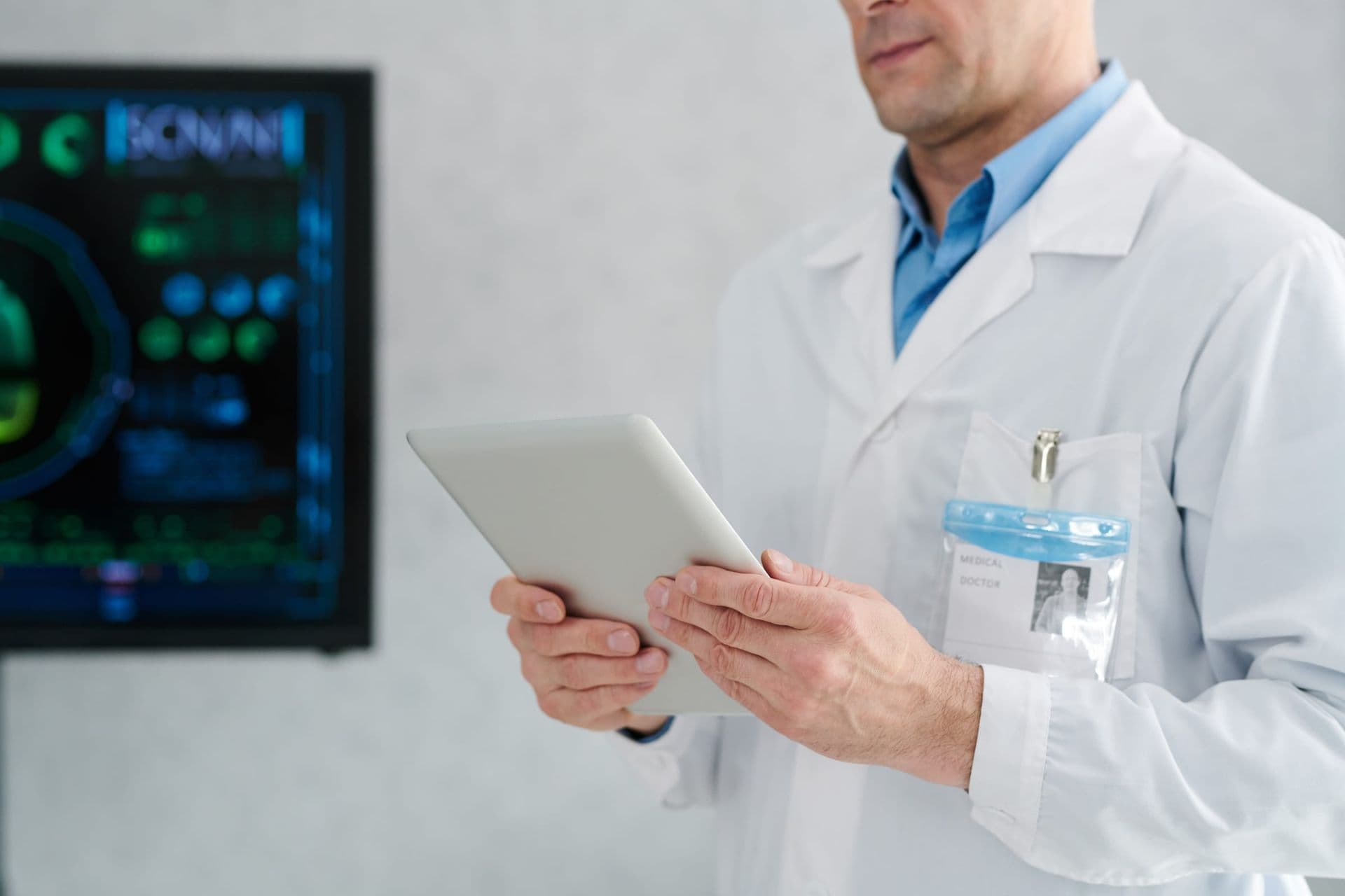 A doctor reviewing information on a tablet in a bright office with screens behind