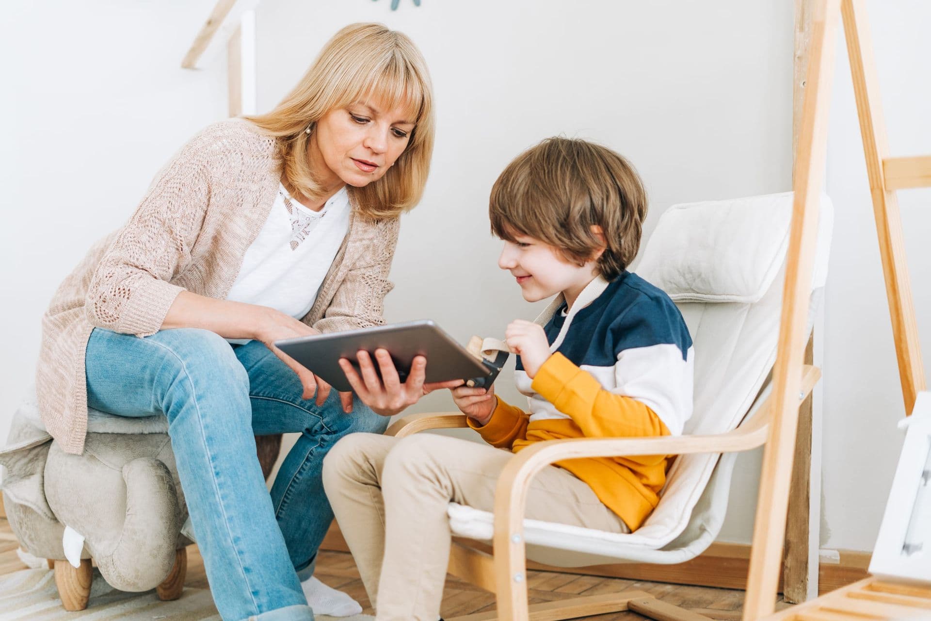 A therapist showing a tablet to a young boy in a bright room